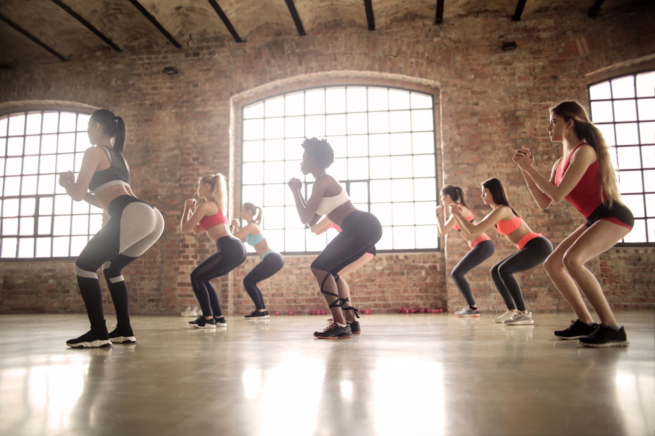 A group of women performing squats in a well-lit fitness studio with large windows.