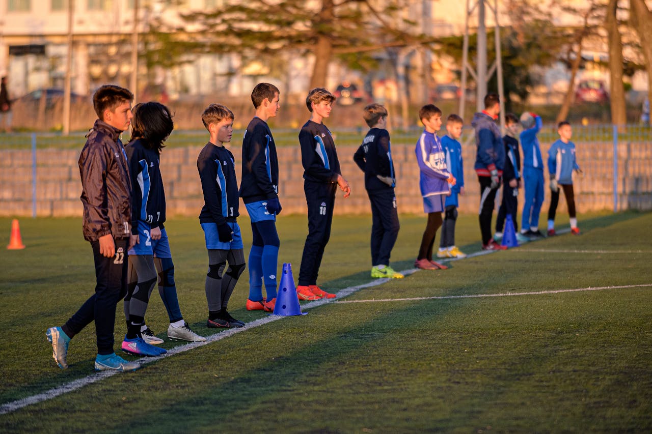 A group of young soccer players lined up on a football field, preparing for a drill at sunset.