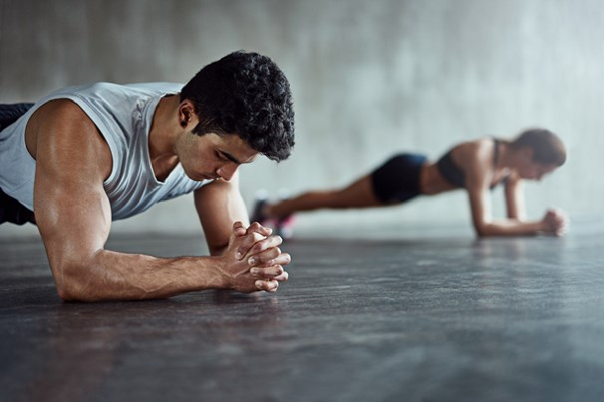 Man and woman holding forearm planks on a gym floor with forearms down.