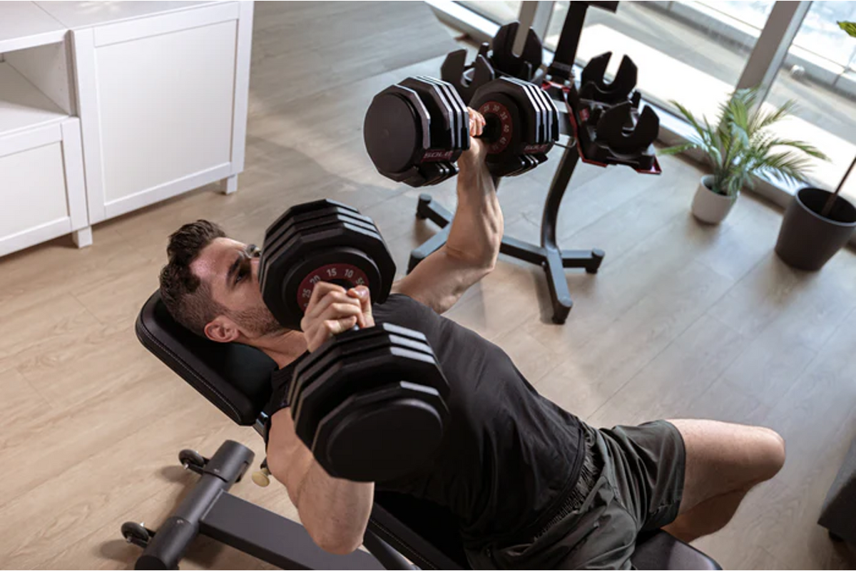 Man performing a heavy dumbbell bench press in a home gym, illustrating the compound pressing movements central to building a Superman-level physique.