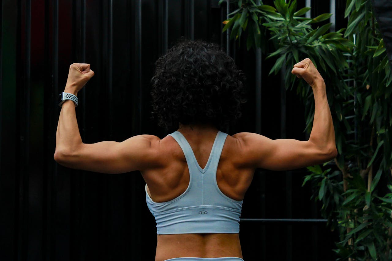 A woman flexing her back and arm muscles, showing strength after a workout.