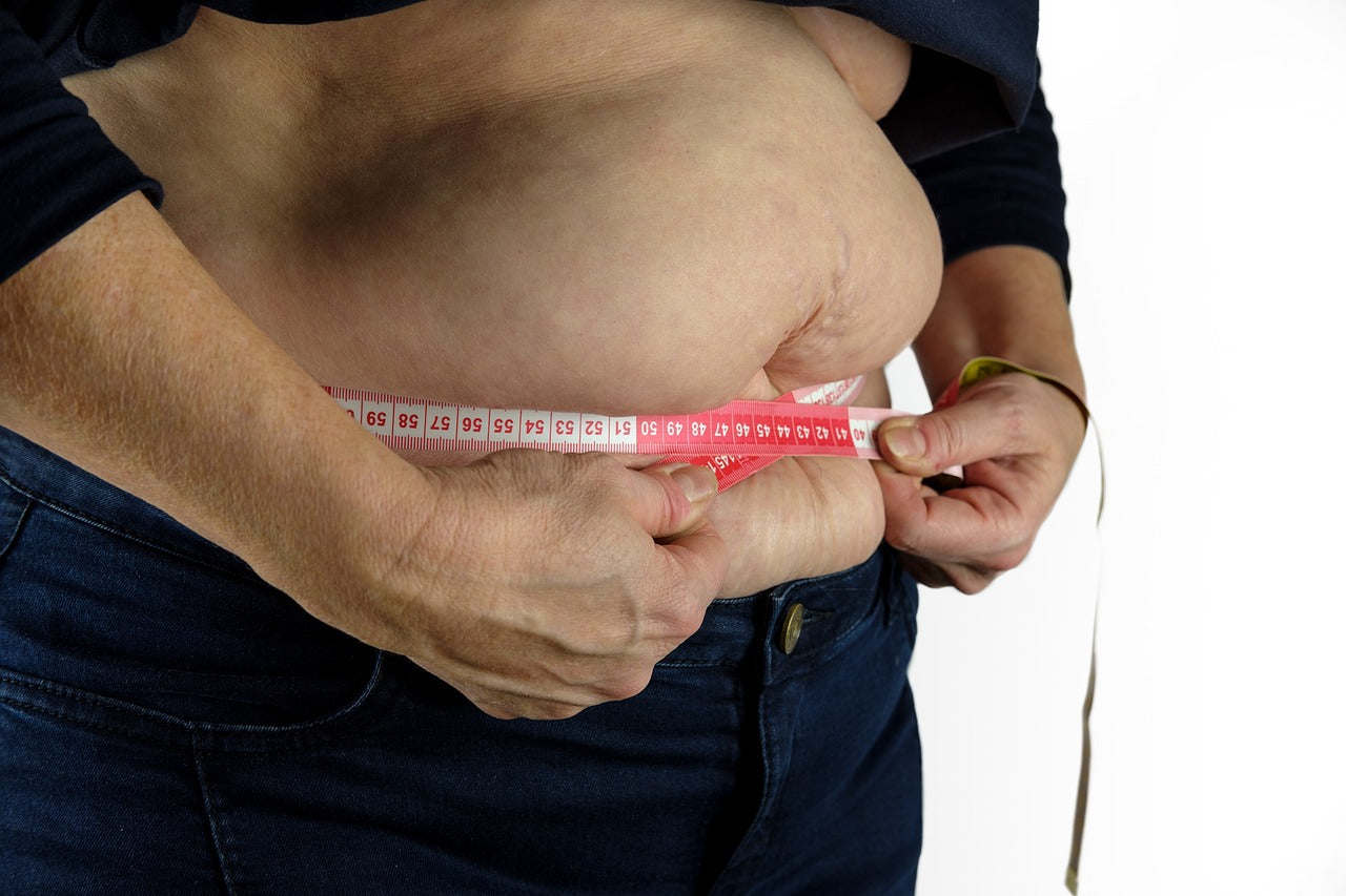 Close-up of person measuring waist with tape measure, focusing on midsection and belly area