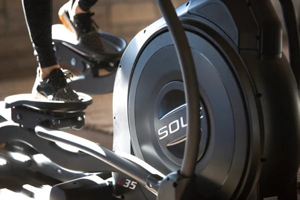 Close-up of person using SOLE E35 elliptical, focusing on flywheel and foot pedals, showcasing smooth operation and joint-friendly design