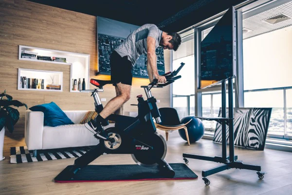 Man in athletic gear riding SOLE exercise bike in living room, focused on workout