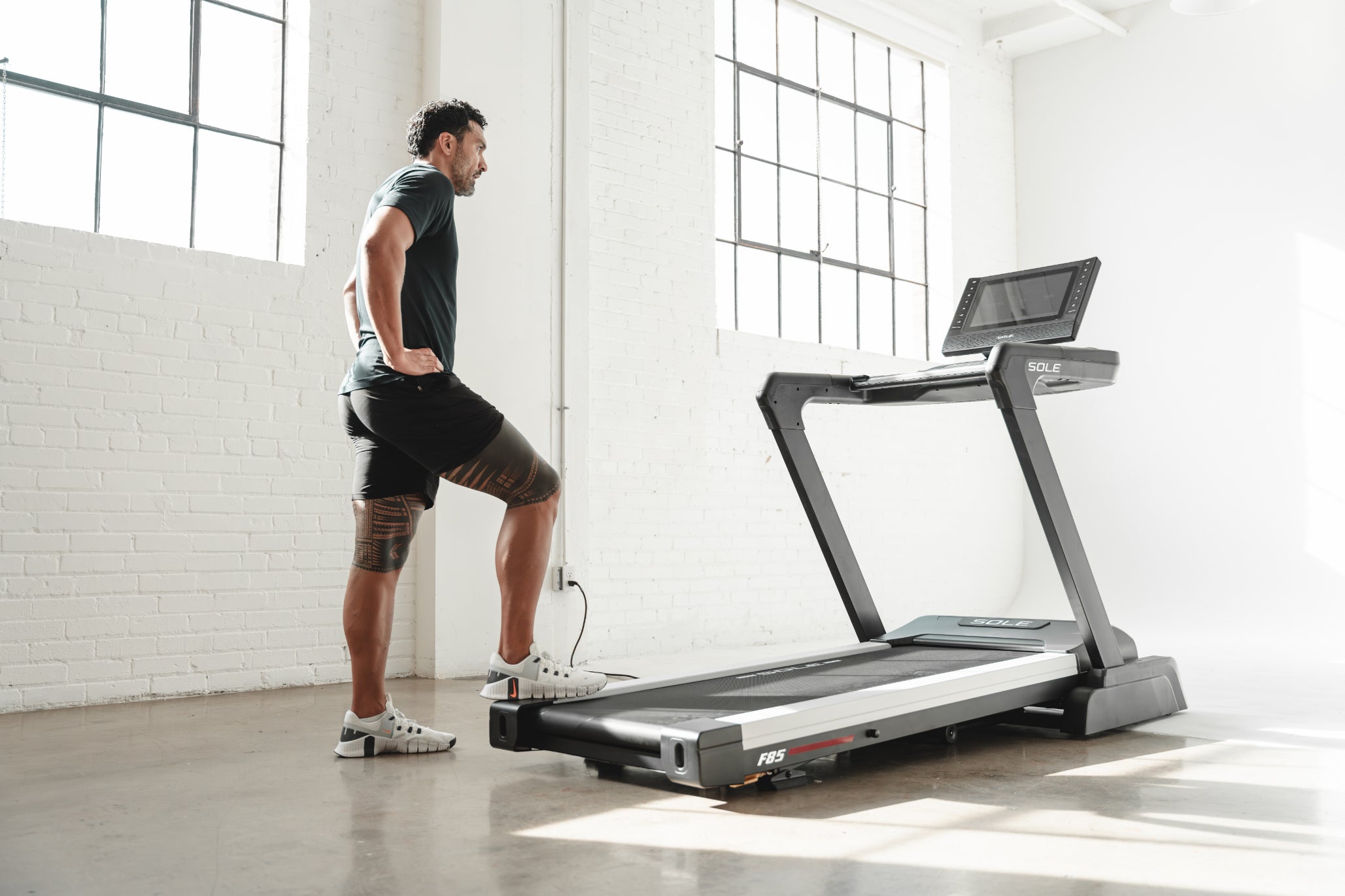 Man standing in front of SOLE F85 treadmill, preparing for workout in bright, minimalist room
