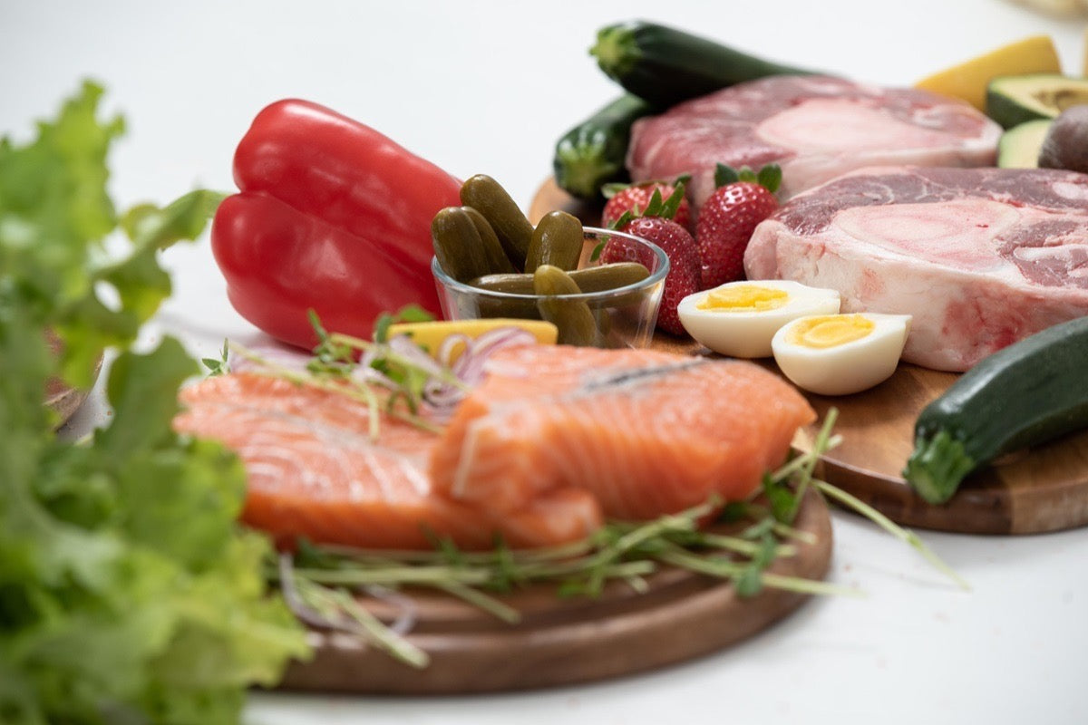 Raw salmon fillets, steaks, boiled eggs, peppers, and leafy greens, showing the whole-food protein sources that form the base of a high-volume training diet.