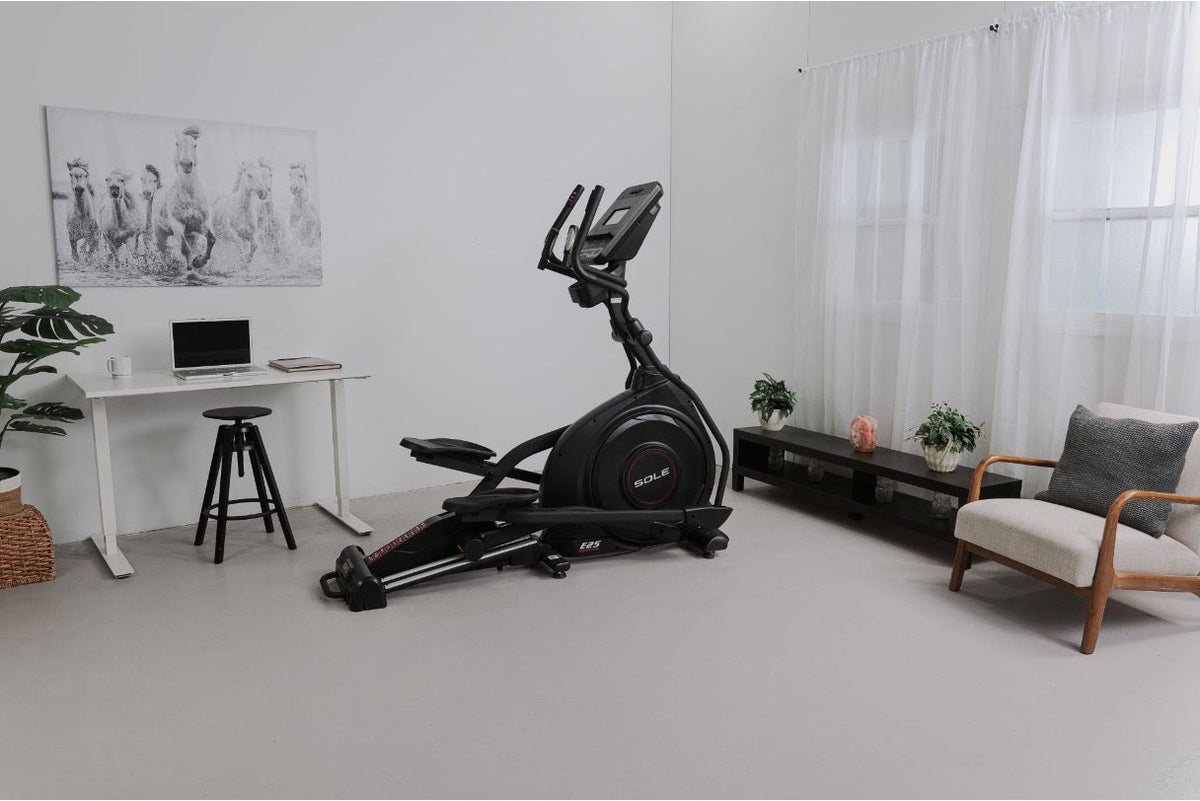 SOLE E25 elliptical positioned in a bright, minimalist living room beside a desk and armchair