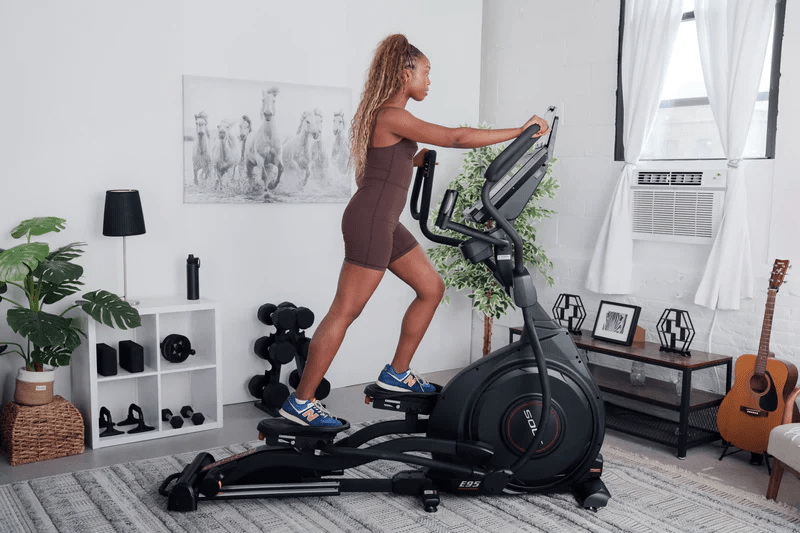 Woman in a brown workout set using a SOLE E95 elliptical trainer in a home gym