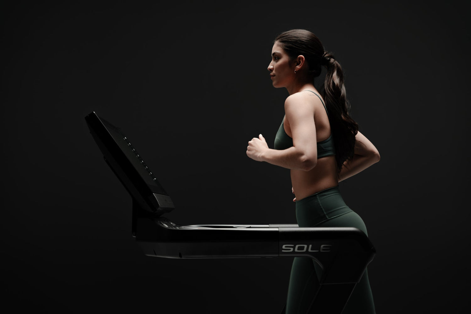 Woman in athletic wear runs on a SOLE treadmill, focusing on cardio and muscle-building.