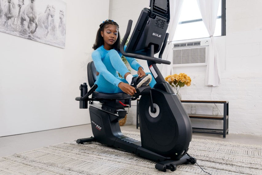 Woman in blue athletic wear securing her foot into the pedal strap of a SOLE R92 recumbent bike
