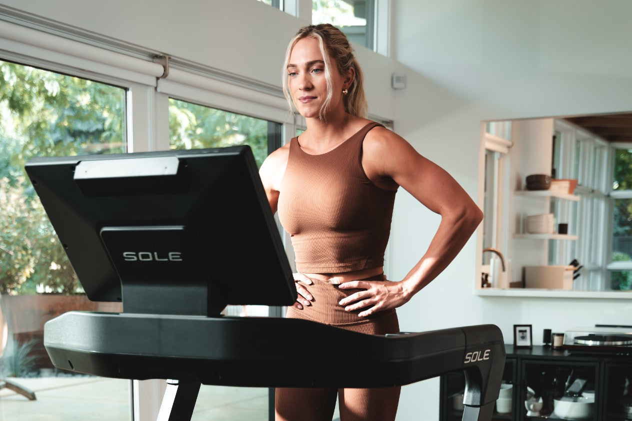 Woman in workout attire uses a SOLE treadmill, focusing on cardio in a gym.