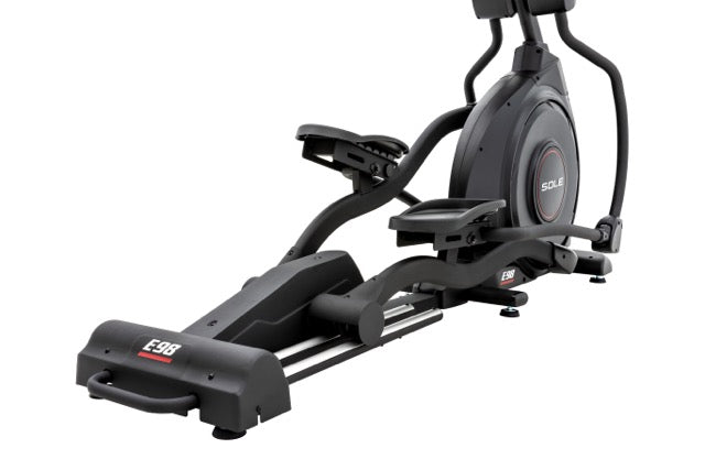 Side view of the Sole E98 elliptical machine, displaying its sleek dark grey design, large central flywheel with the SOLE logo, adjustable foot pedals, and handlebars, all set against a white background.