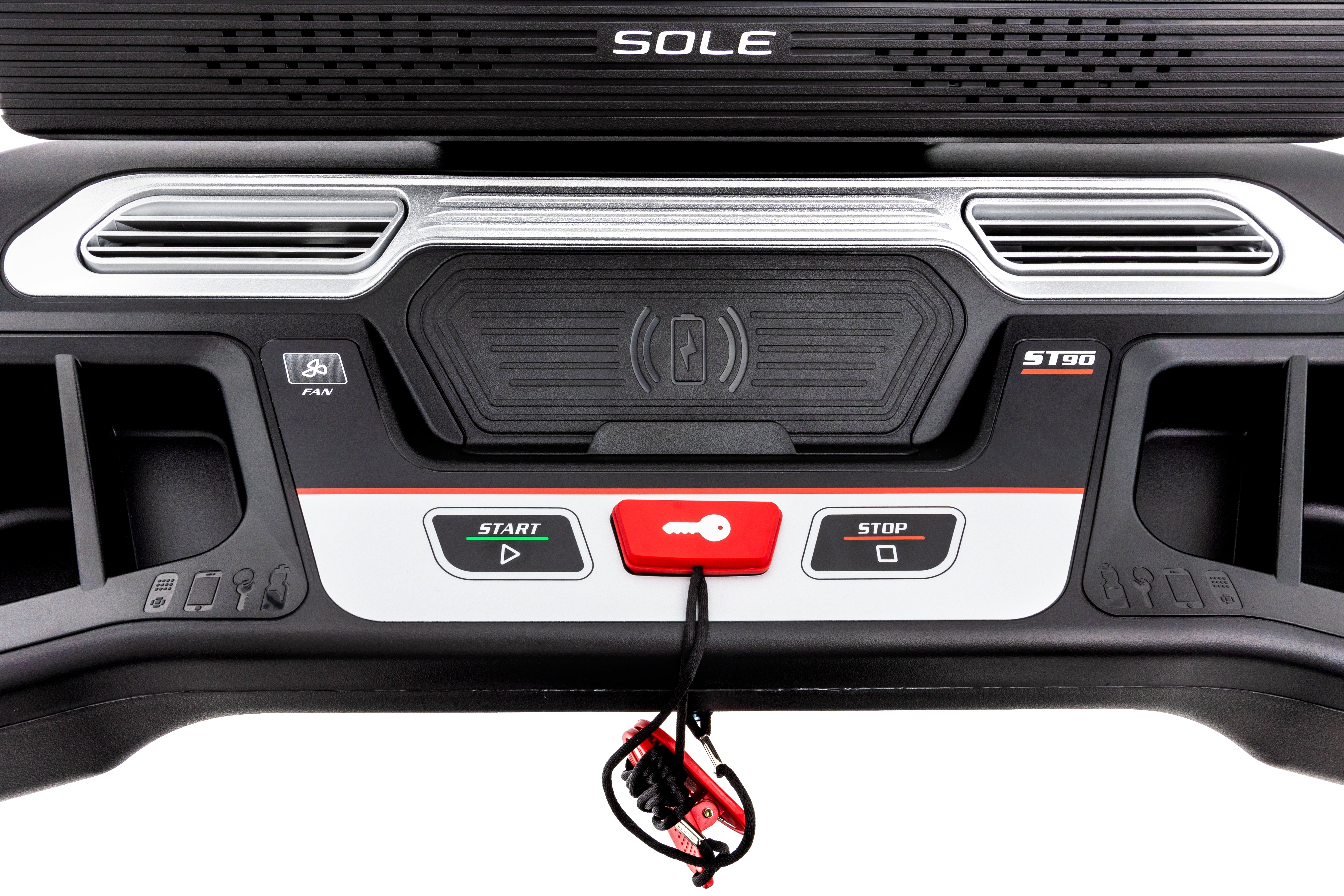 Frontal view of the Sole ST90 treadmill's control interface, highlighting the brand logo, speaker grills, start and stop buttons, and a safety key tether on its polished black and silver surface.