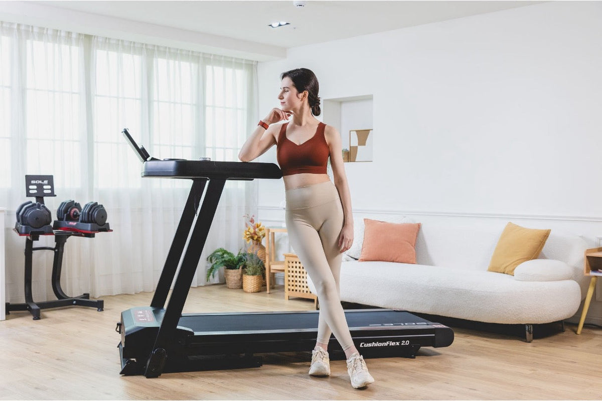 A fitness model standing by a SOLE Fitness treadmill after completing 20K steps