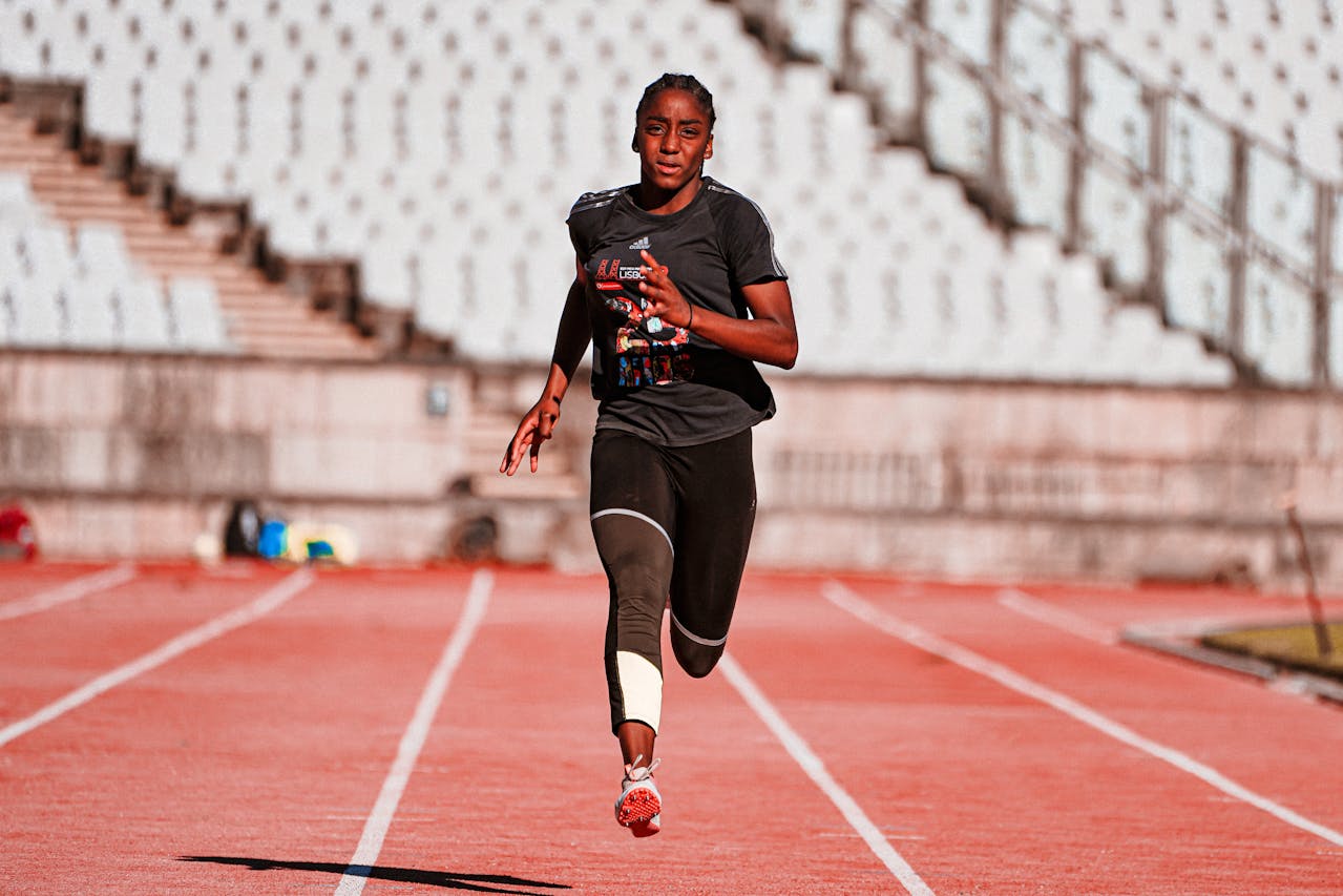 A focused athlete sprinting on an outdoor track, wearing athletic gear.