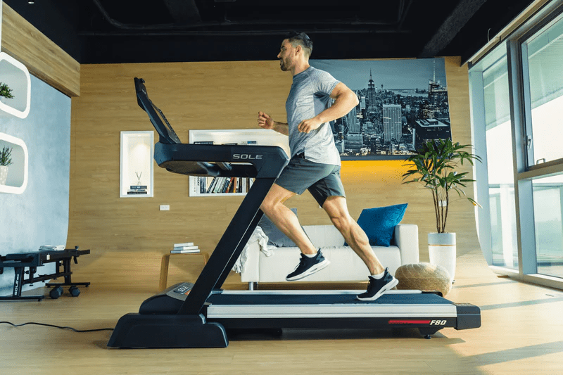 A man running on the SOLE F80 treadmill in a modern living room setting.