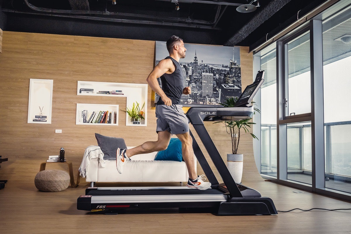 A man runs on the SOLE F85 treadmill in a modern apartment setting
