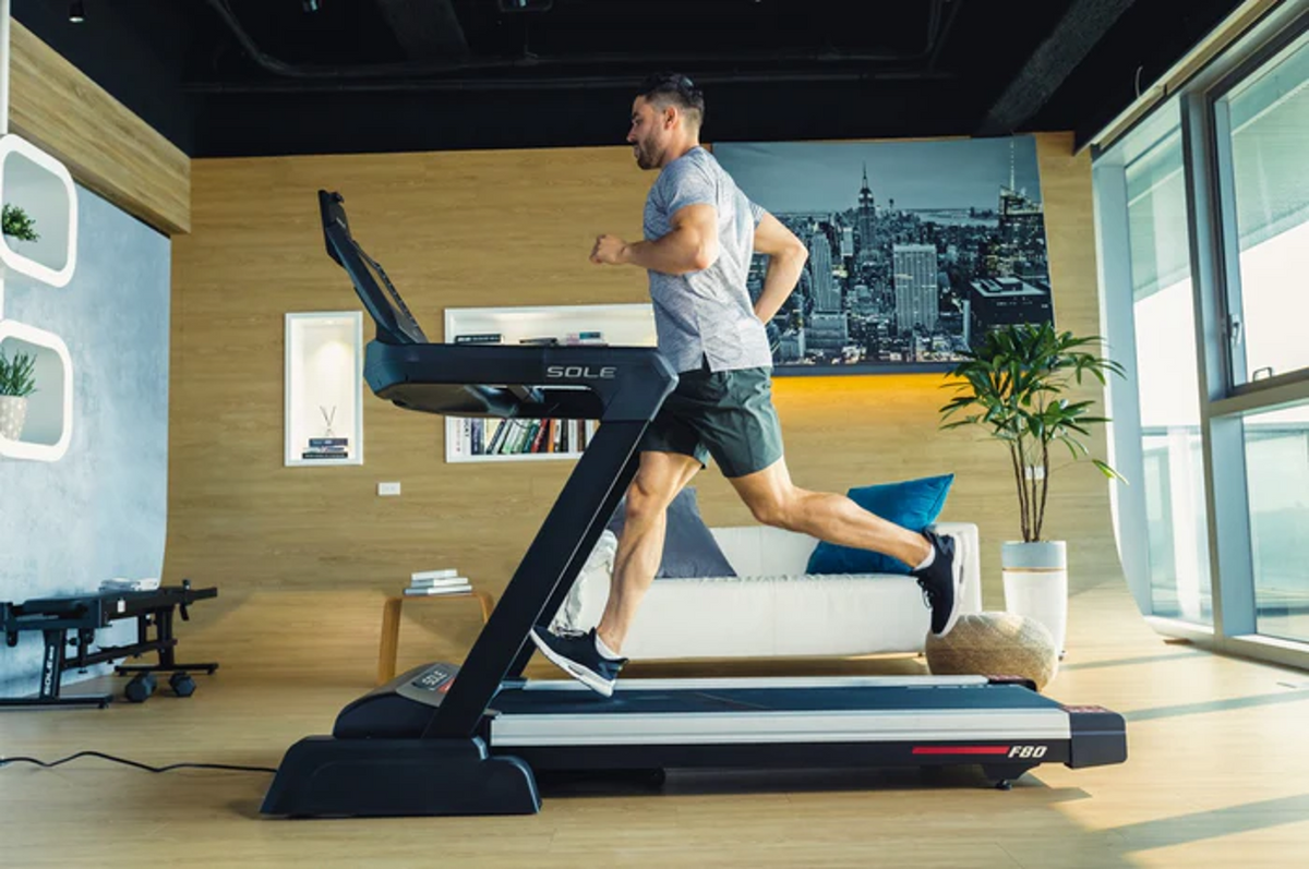 Athletic man running at full stride on the black SOLE F80 treadmill in a modern home setting