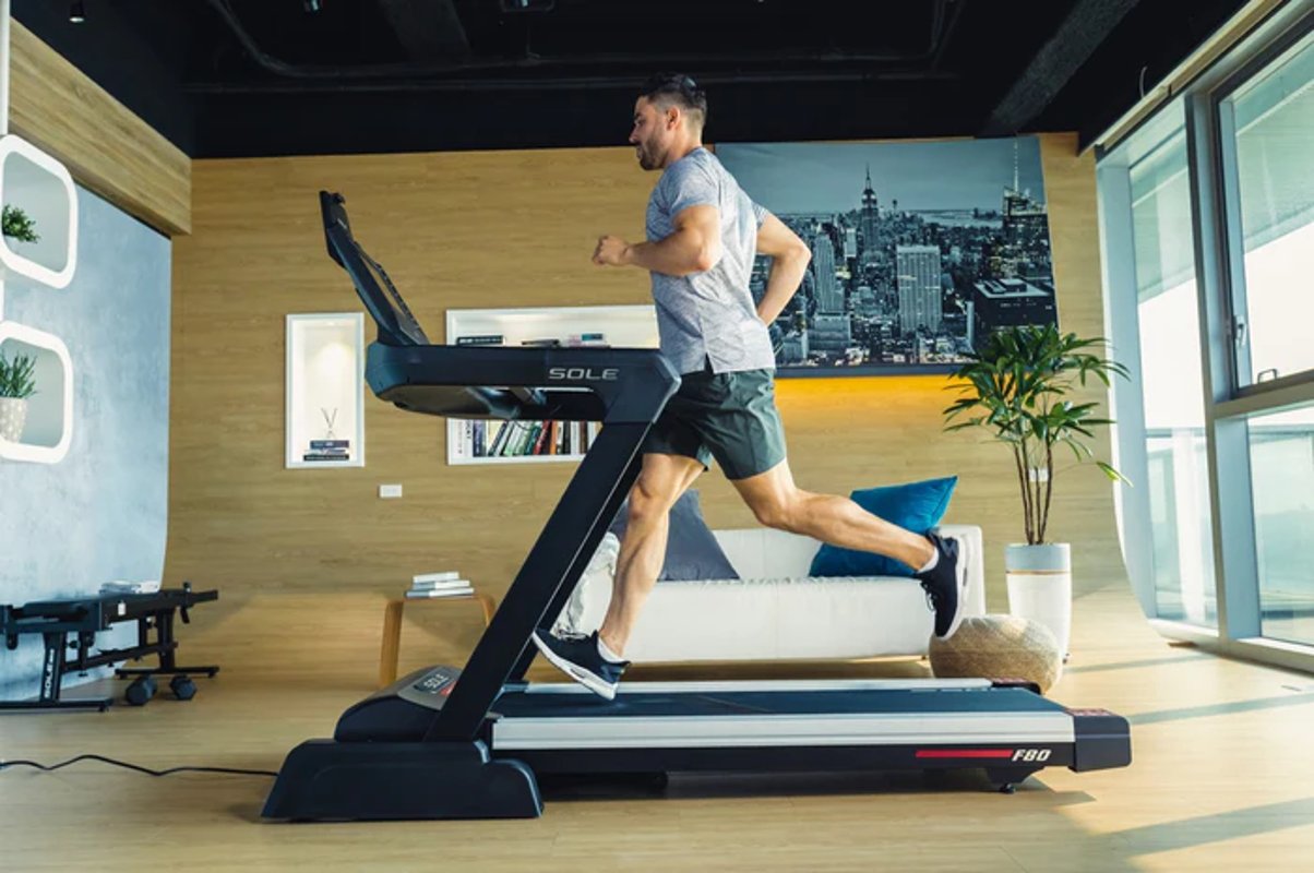 Athletic man running at full stride on the black SOLE F80 treadmill in a modern home setting