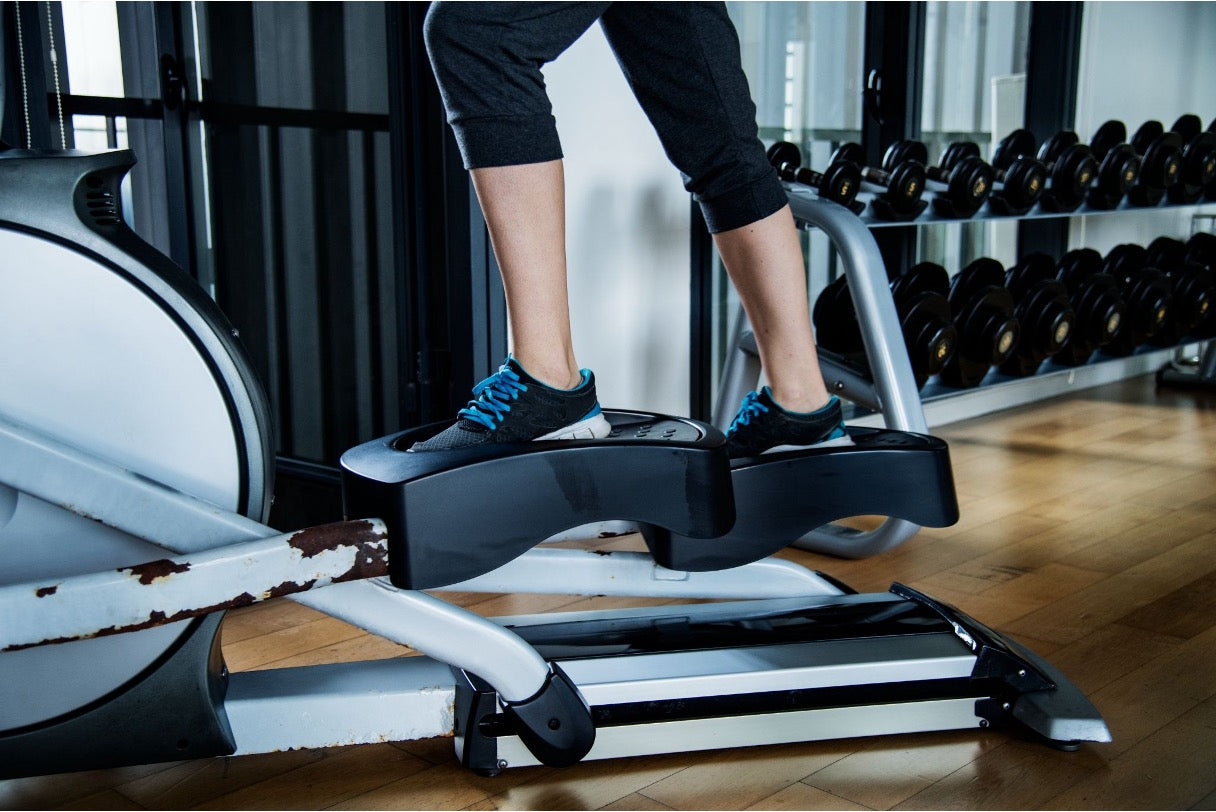 A user exercising on an older elliptical trainer with visible paint wear on its metal base frame