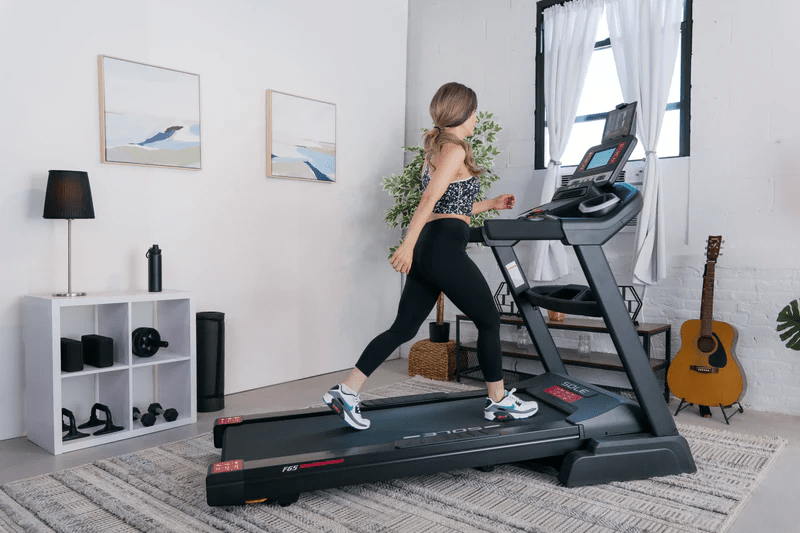 A woman walking on a SOLE F65 treadmill in a bright, minimalist home gym setup