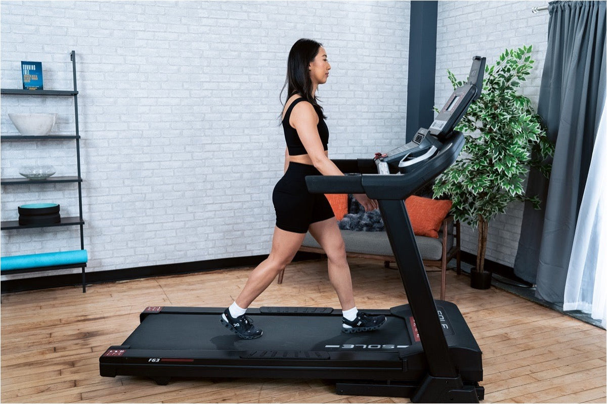 A woman walks at a steady pace on a SOLE F63 treadmill, hands off the rails and posture upright through the stride.