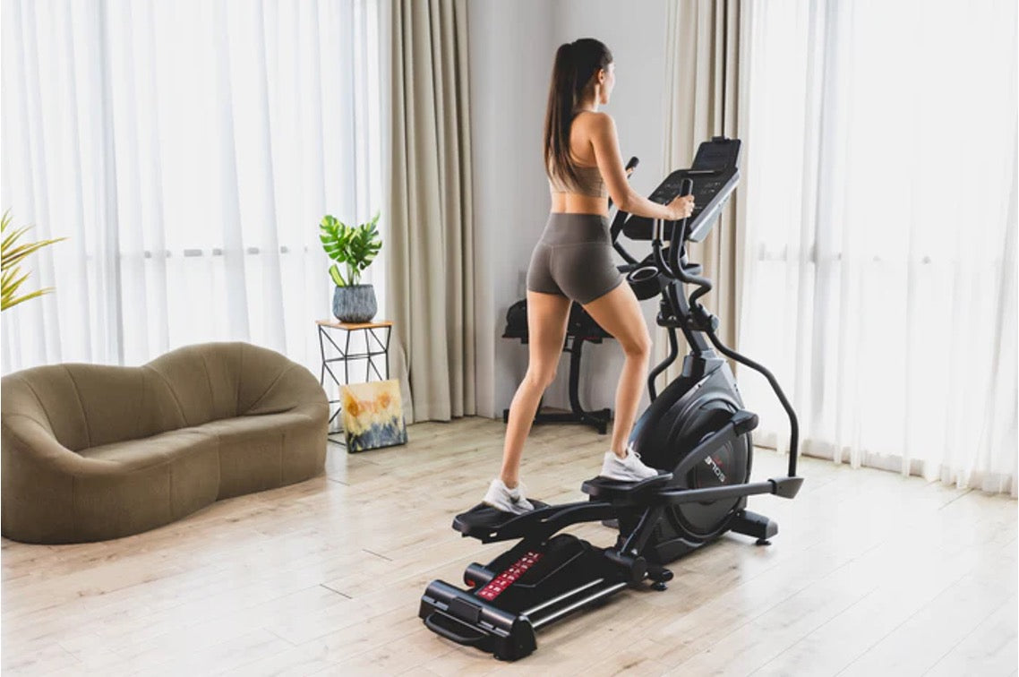 Woman working out on a SOLE elliptical in a sunlit living room, showing smooth low-impact cardio for joint-friendly exercise at home