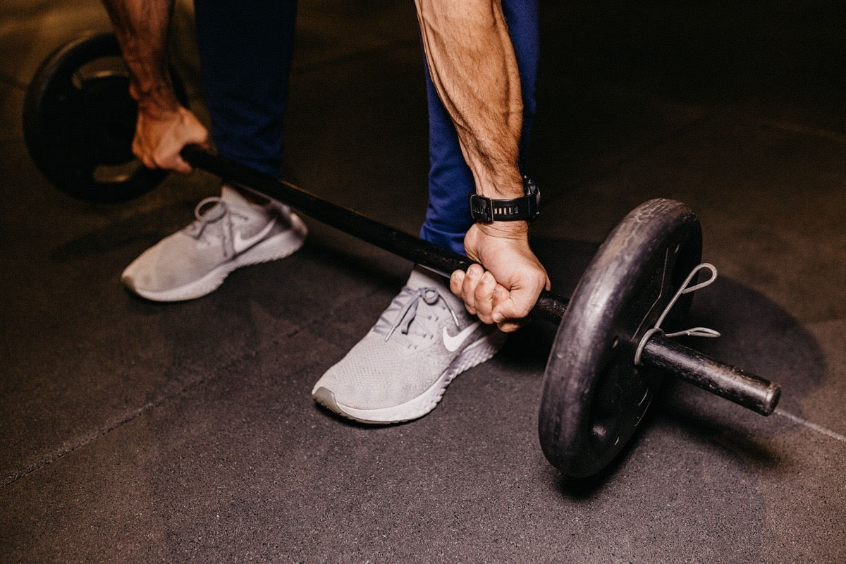 Close view of a lifter gripping a loaded barbell, the kind of compound lifting behind the Tom Hardy Bane workout