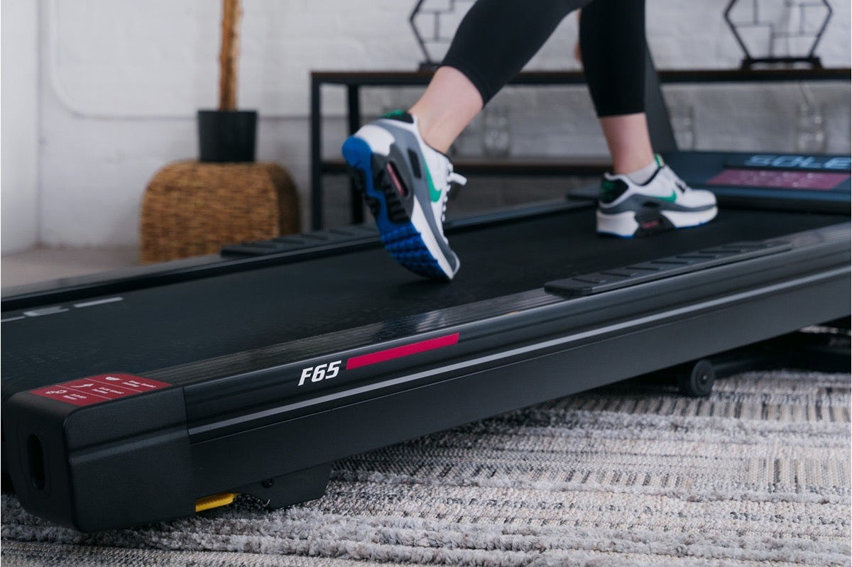 Close view of a walker's feet mid-step on a SOLE F65 belt, heel landing first through a steady walking stride