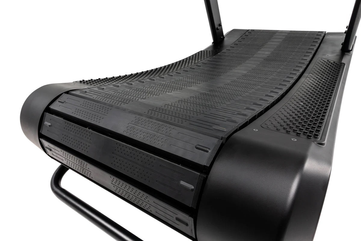 Curved manual treadmill deck highlighting the textured black running belt and rounded front roller that enables self-powered motion