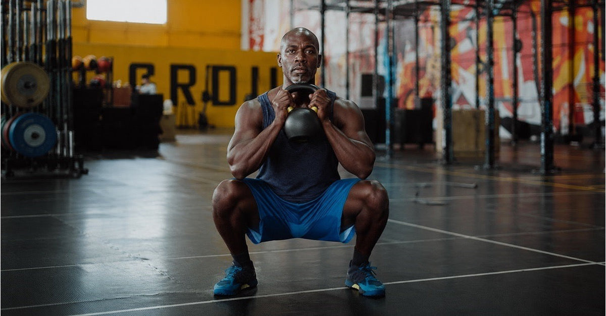 Man holding a kettlebell at chest height in the bottom position of a goblet squat, torso upright and thighs parallel to the floor