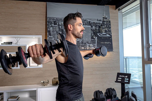 Man performing a standing dumbbell fly with SOLE SW180 Adjustable Dumbbells.