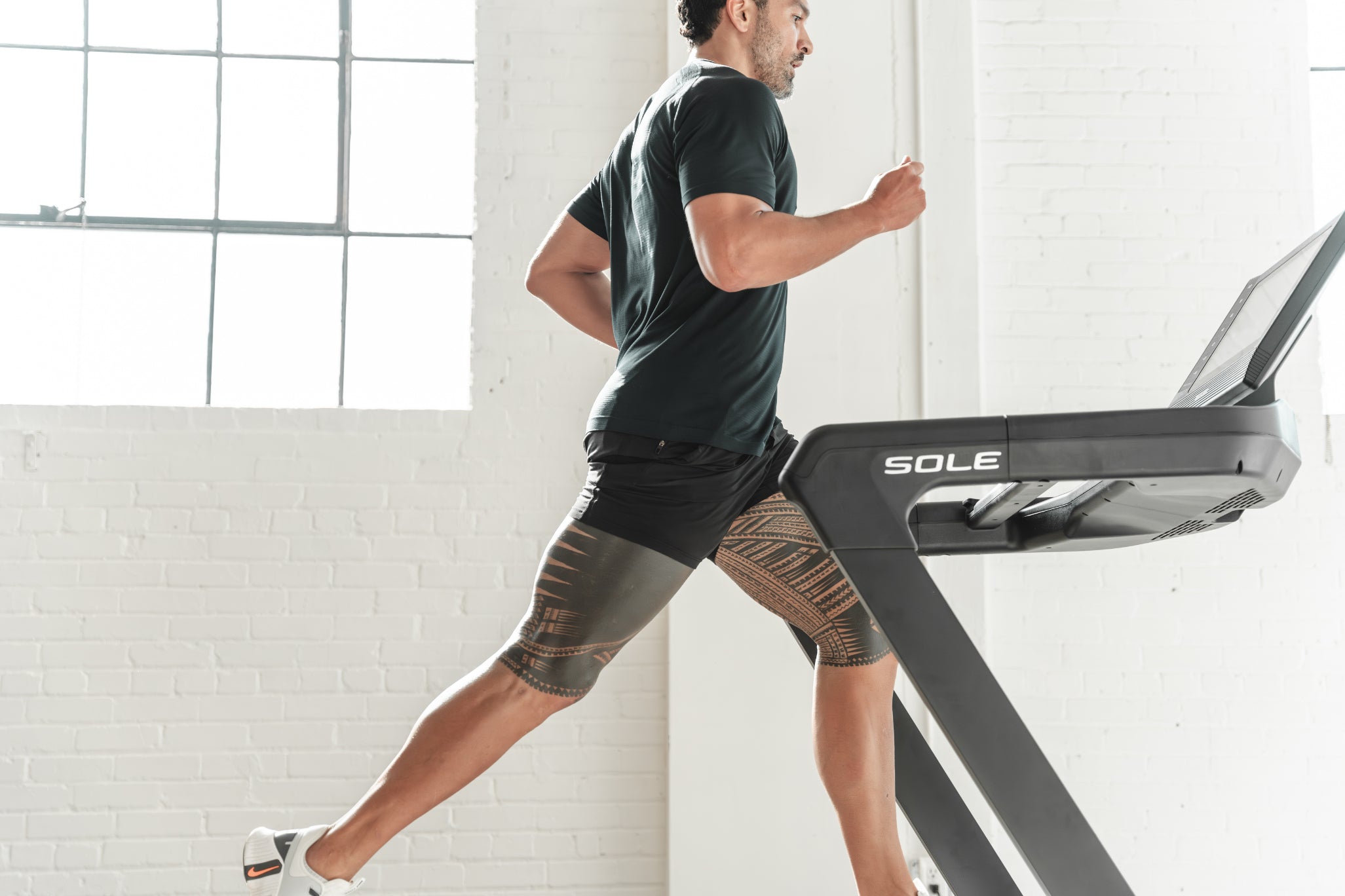 Man running on SOLE F85 treadmill in a bright room with large windows, showcasing the treadmill’s design and performance.