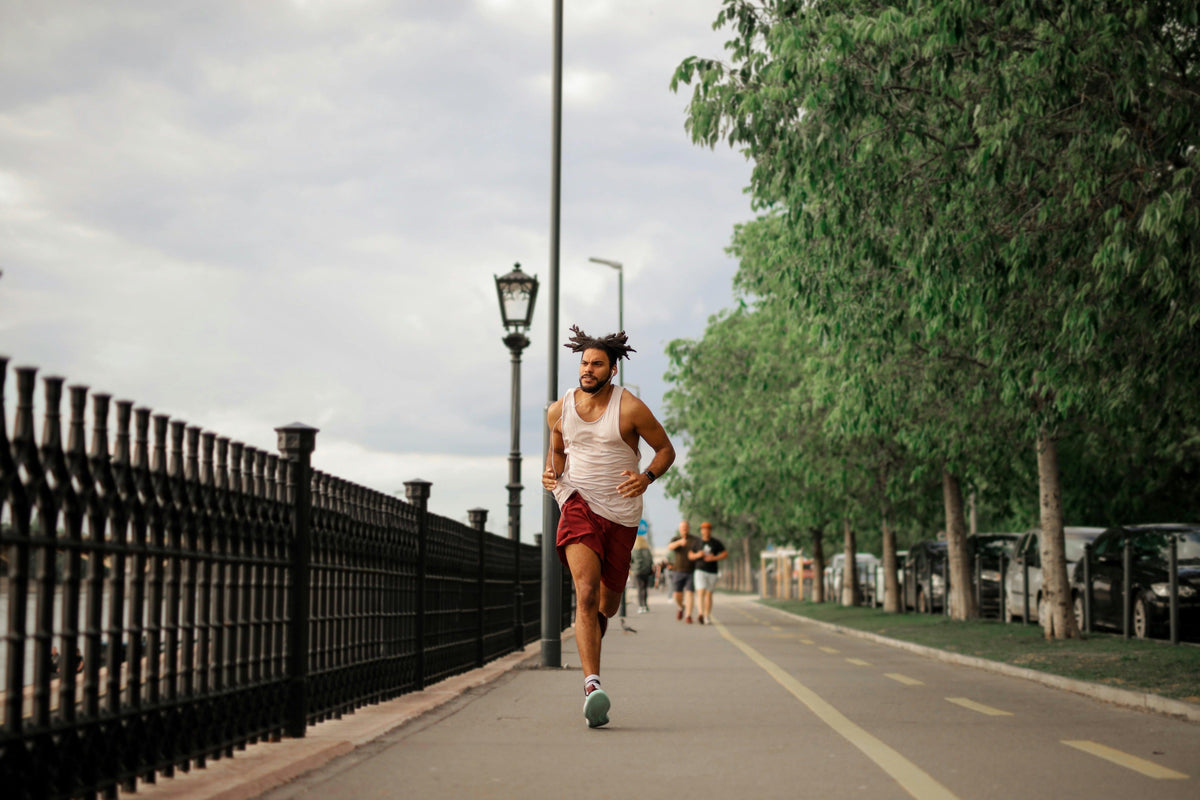 Man runs along a tree-lined path with a fence on one side and others in the background.