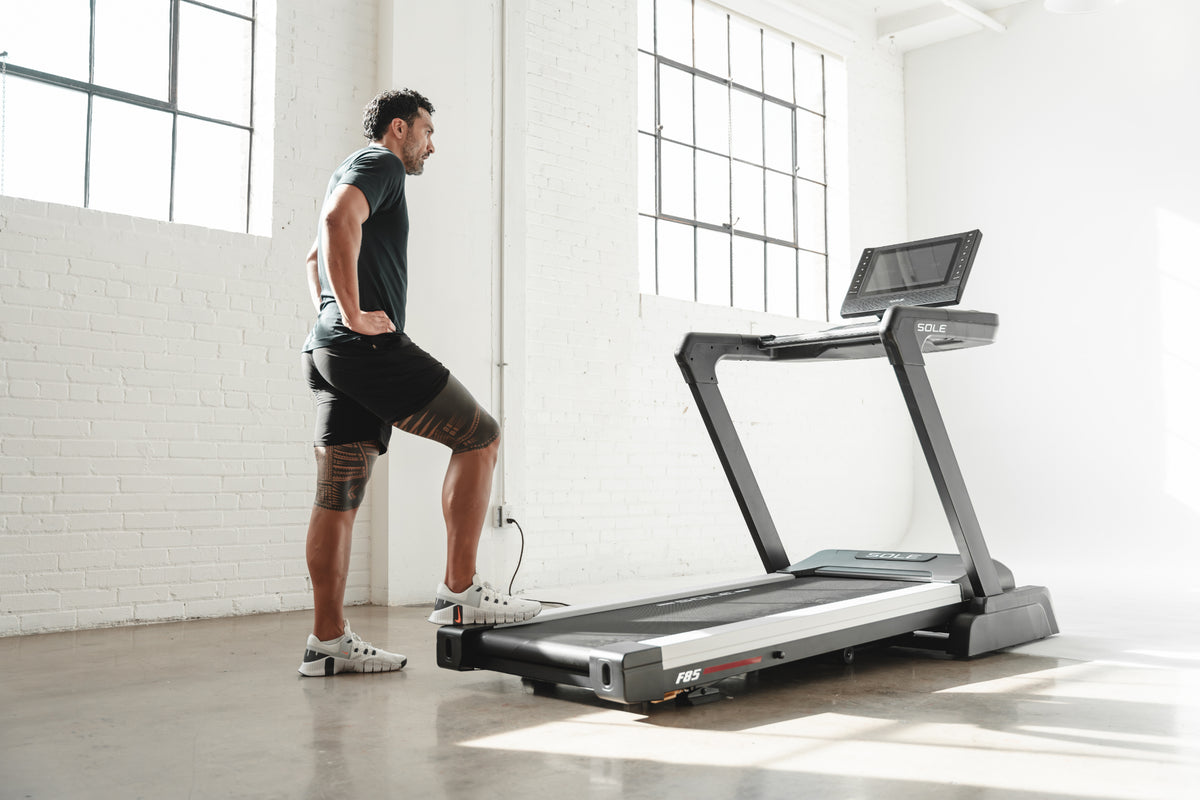 Man standing in front of SOLE F85 treadmill, preparing for workout in bright, minimalist room