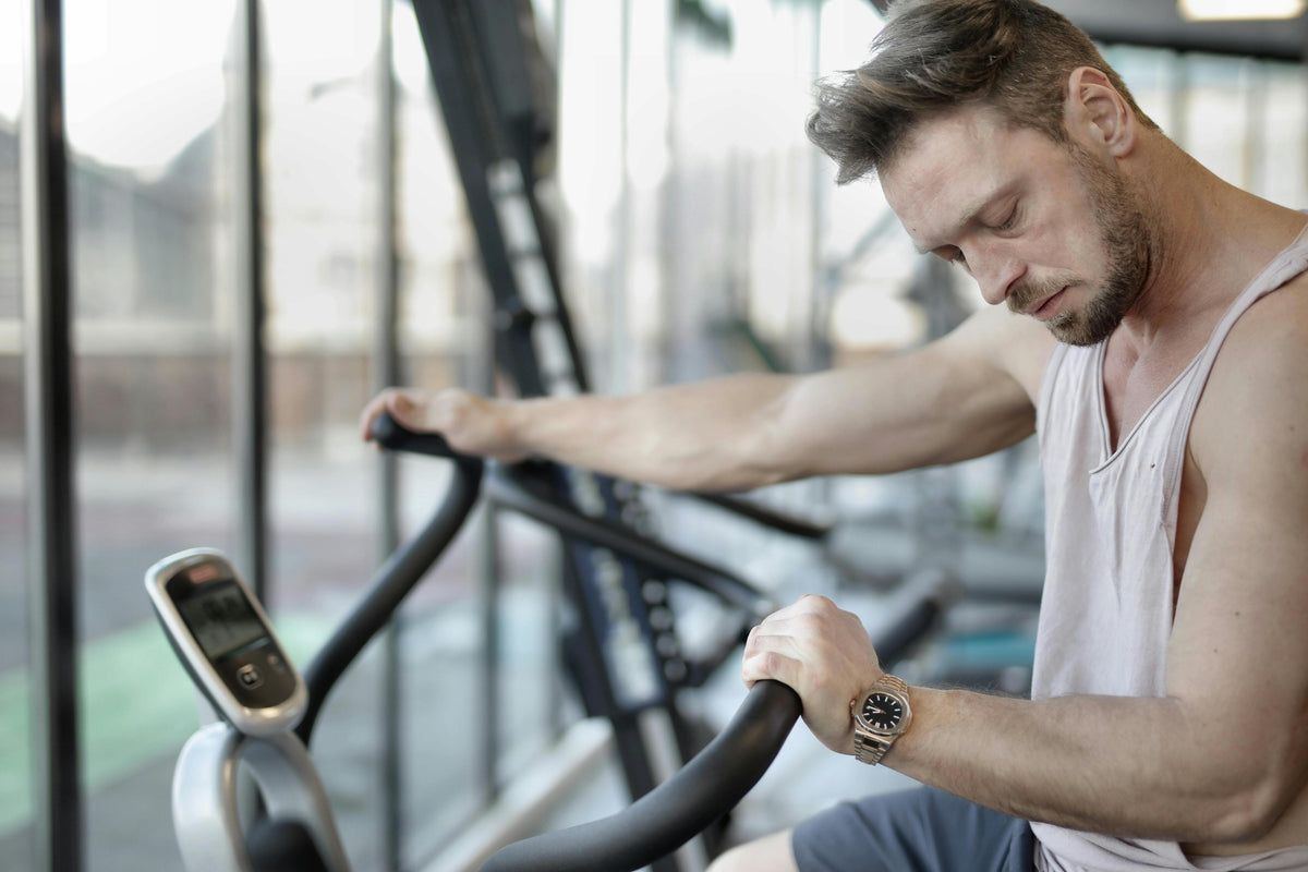 Man wearing tank top in gym, leaning on handlebars of elliptical machine