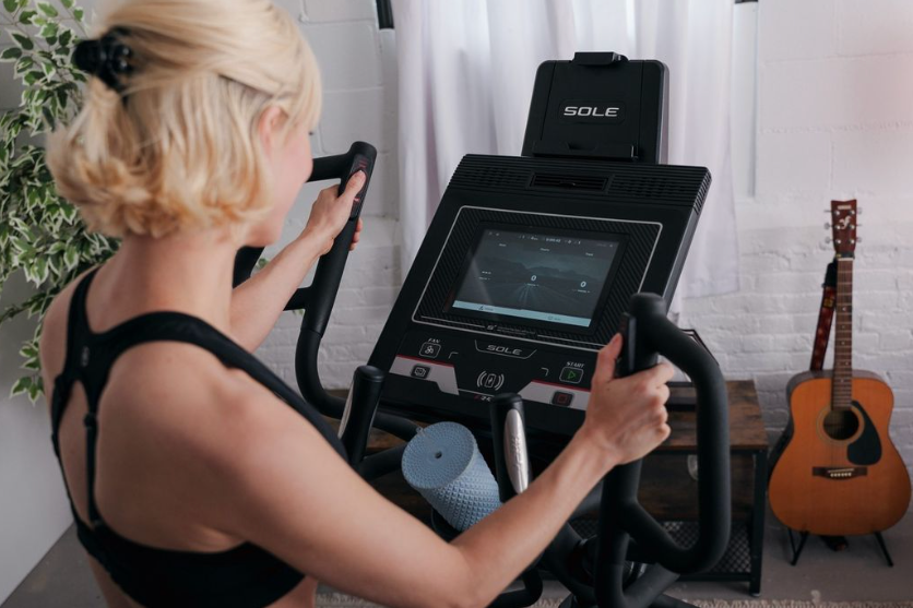 Woman exercises on SOLE E35 Elliptical machine, focusing on cardio in a home fitness space.
