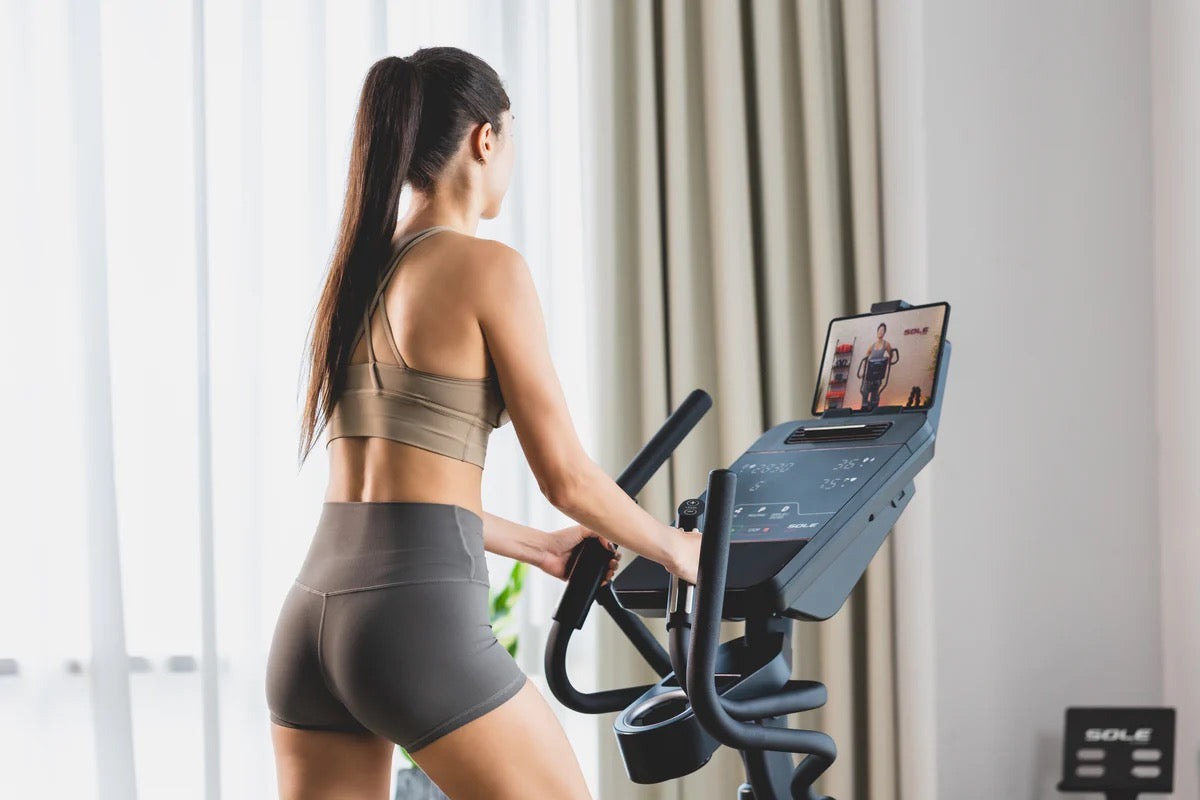 Woman exercising on a SOLE elliptical at home, streaming a guided workout class on its built-in touchscreen