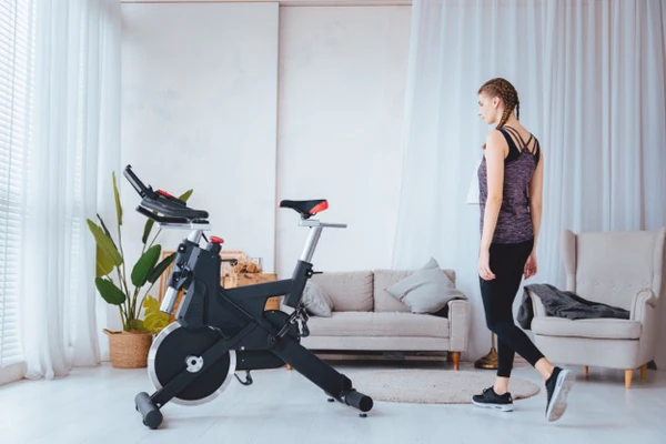 Woman in workout clothes stands next to a SOLE exercise bike in the living room.