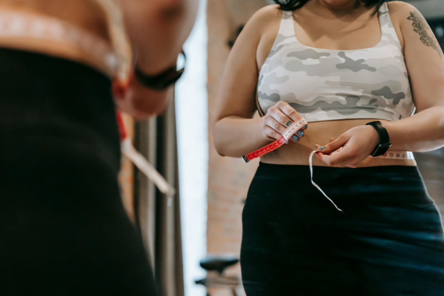 Woman measuring waist with a tape measure, highlighting importance of tracking calorie count for weight management.