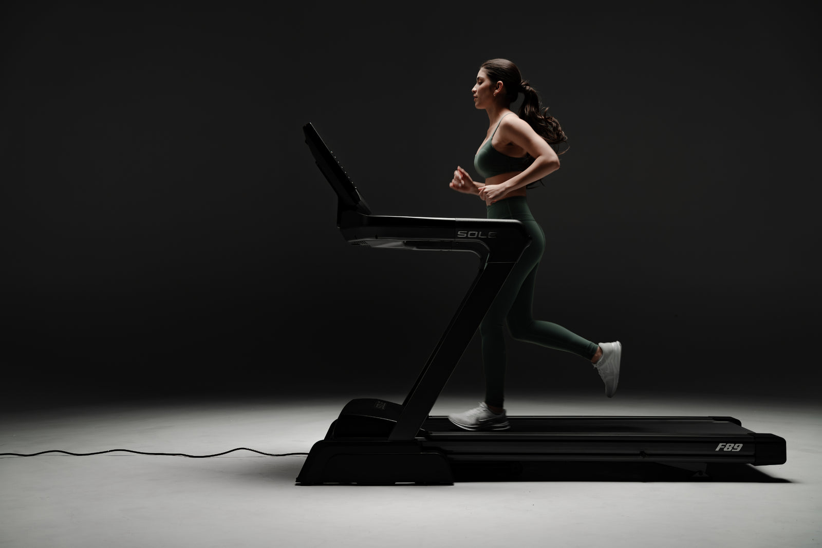 Woman running on SOLE F89 treadmill in sleek, dark studio, highlighting treadmill's modern design.