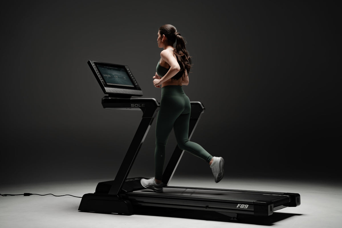 Woman running on SOLE F89 treadmill, showcasing sleek design and advanced features for high-quality workout experience.