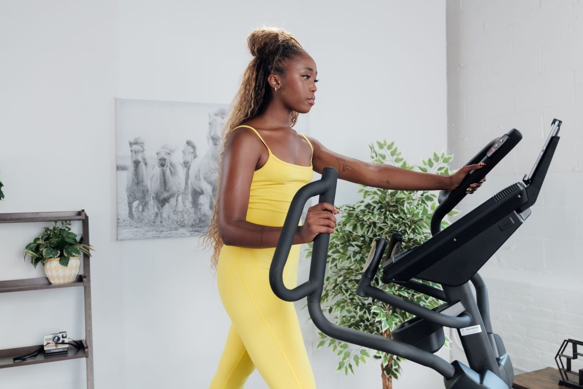 Woman using a SOLE elliptical with hands on the moving handlebars mid-stride