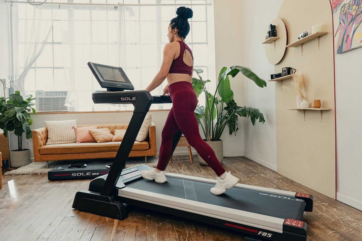 Woman walking at a brisk pace on a SOLE F85 treadmill in a sunlit living room