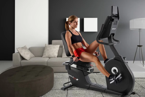 Woman working out on SOLE LCR Recumbent Bike in living room, focusing on building strength and toning muscles.