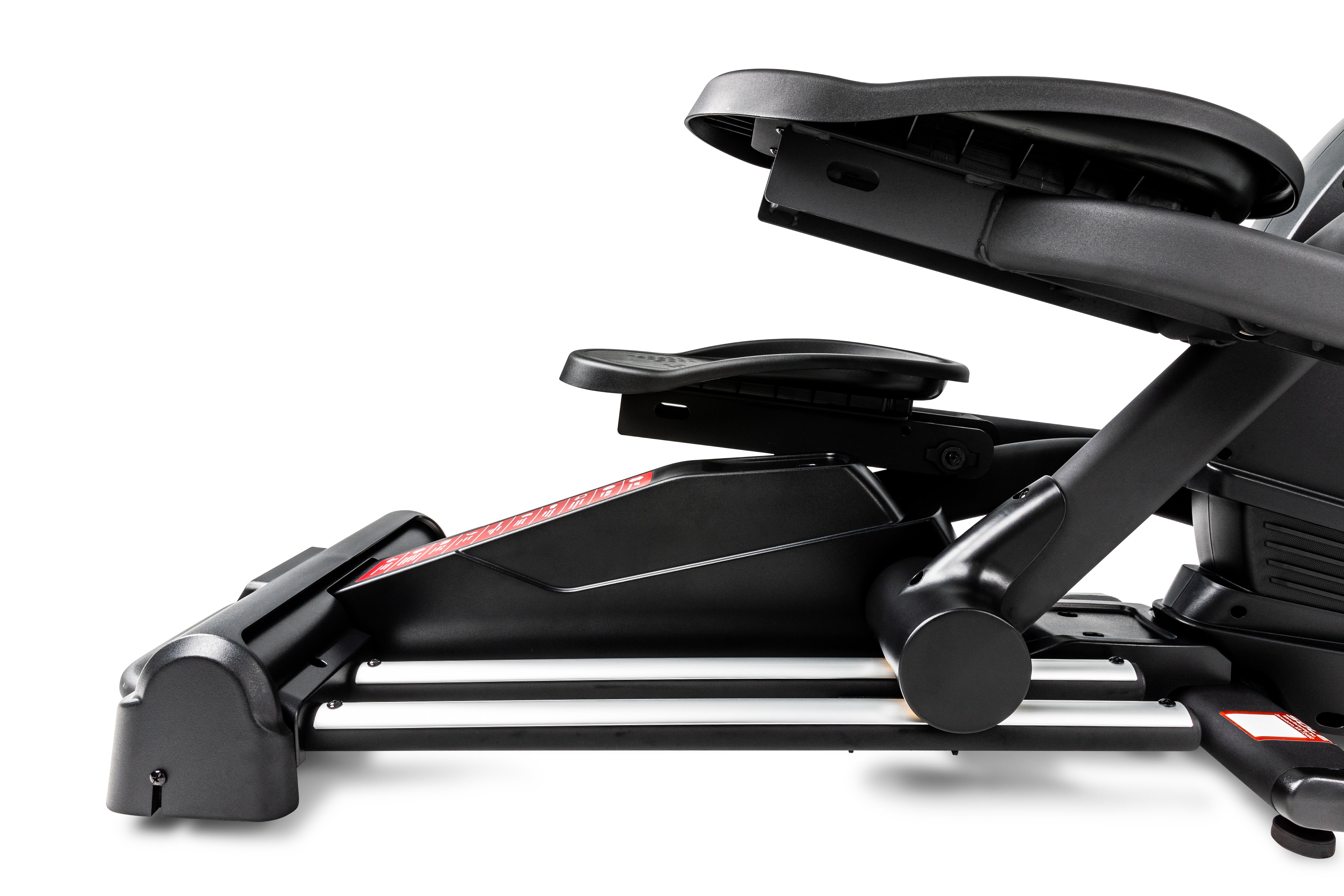 Angled view of the Sole E25 elliptical machine, highlighting its foot pedals, base frame, handlebars, and the black and gray design with red branding details.