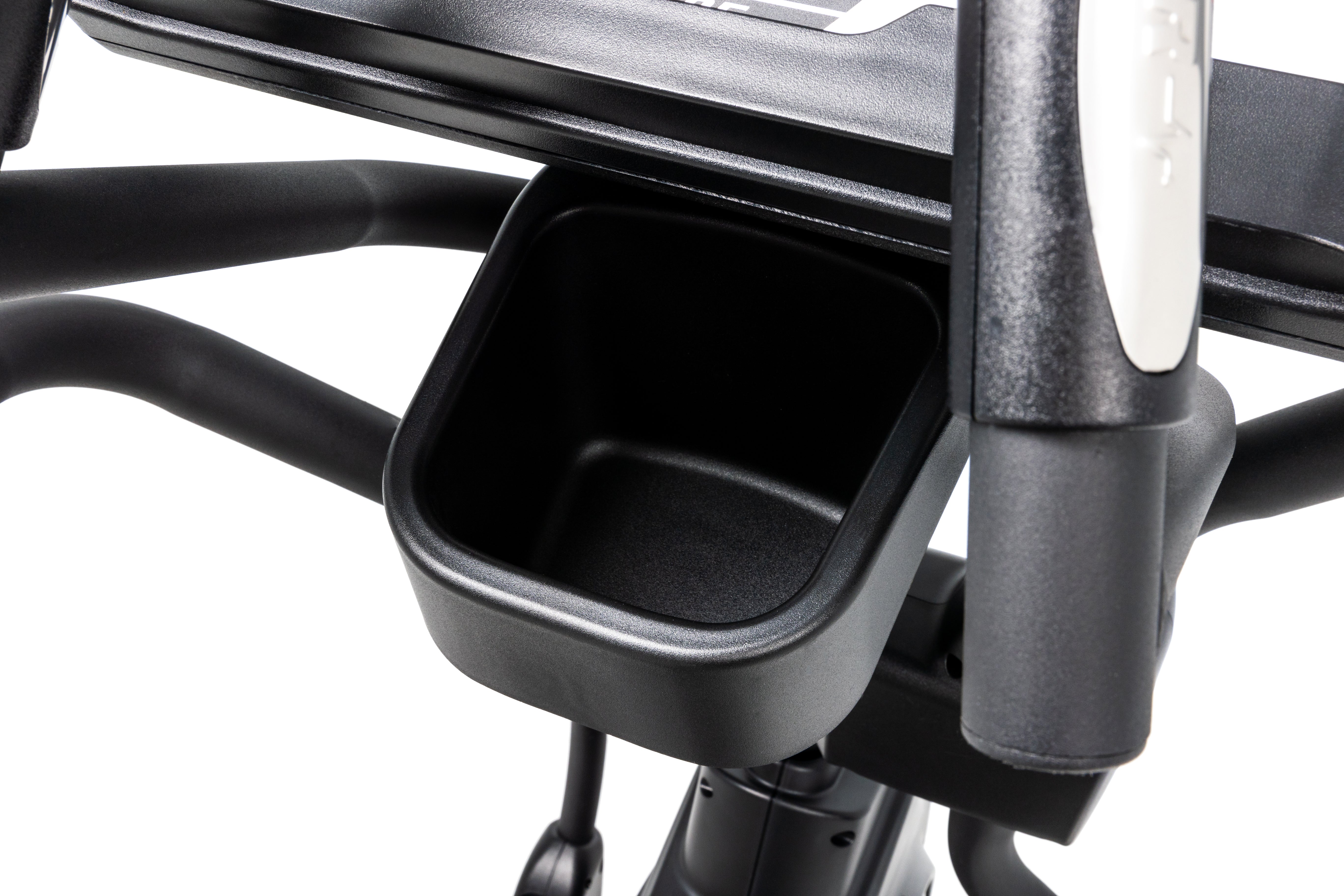 Close-up view of the Sole E95 elliptical trainer's accessory holder, showcasing its deep black storage compartment, a section of its padded foot pedal, and the textured handgrip with a white adjustment button.