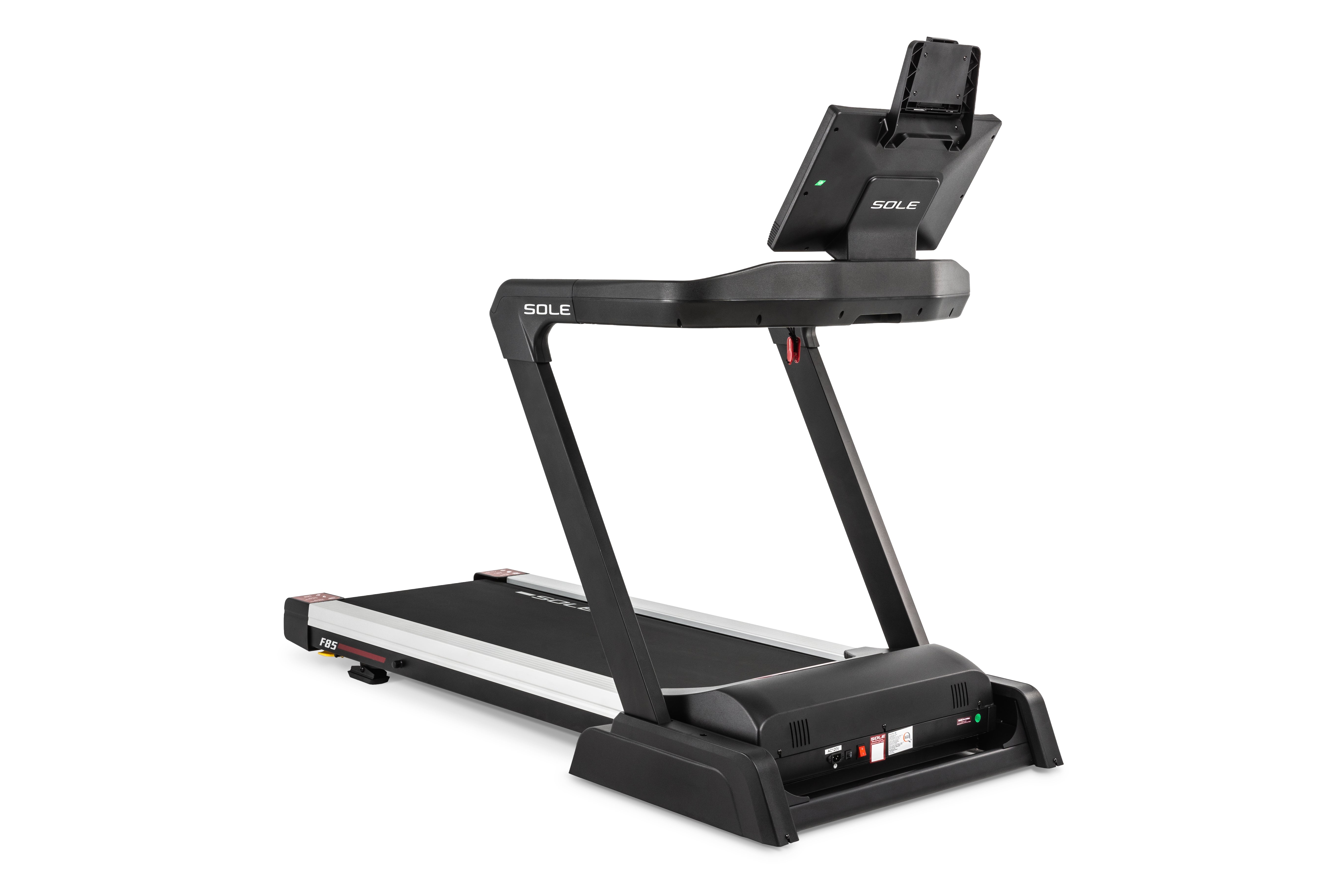 Angled view of the Sole F85 treadmill featuring a black frame with "SOLE" branding, a digital display with an attached tablet holder, and a spacious running belt. The deck showcases the "F85" logo and red accents, and the base has built-in controls and safety features.