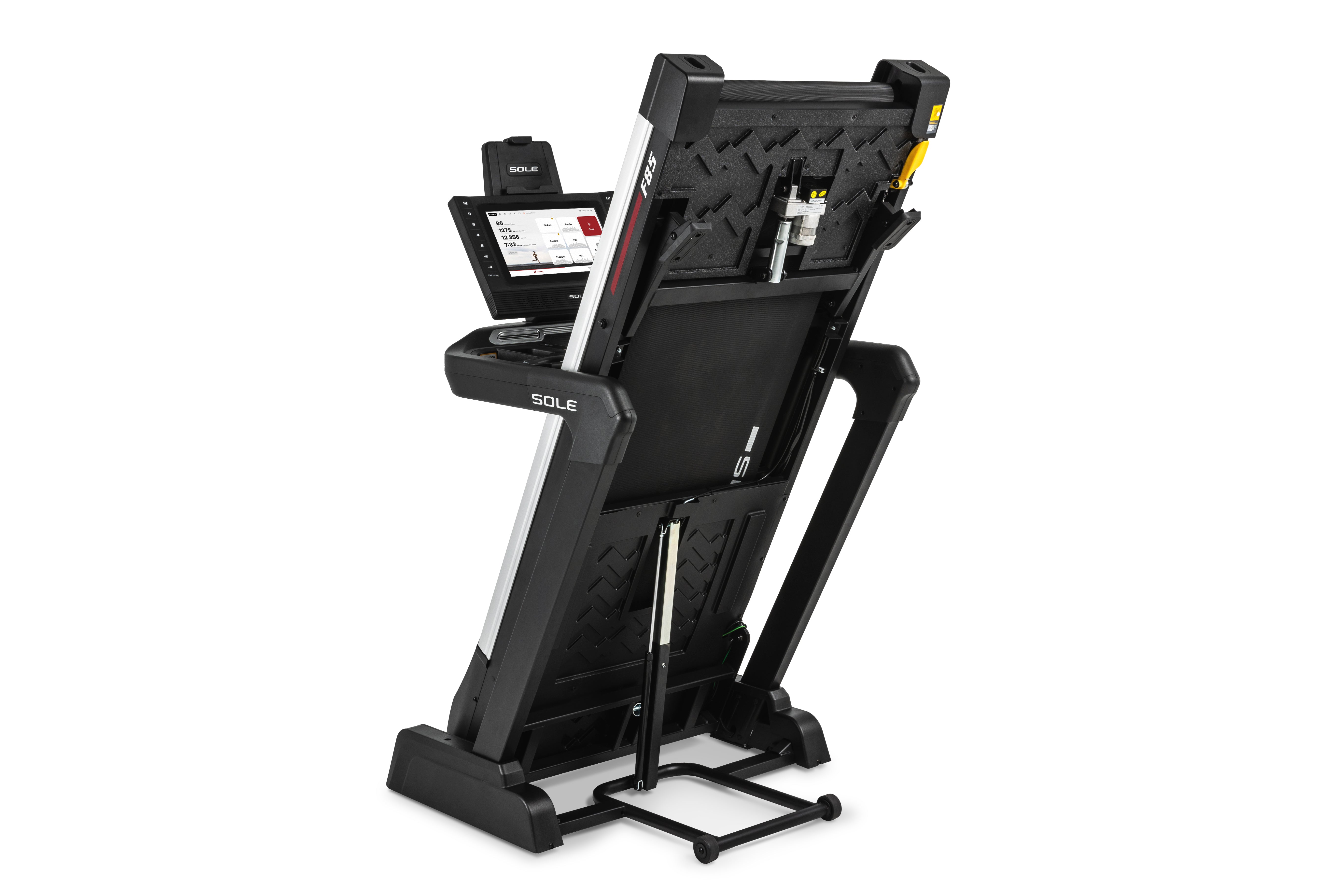 Sole F85 treadmill in a folded upright position, displaying its black textured underside, hydraulic folding mechanism, and front-mounted wheels for mobility. The side panel includes the SOLE logo and a control panel with a digital display is visible on the top right.
