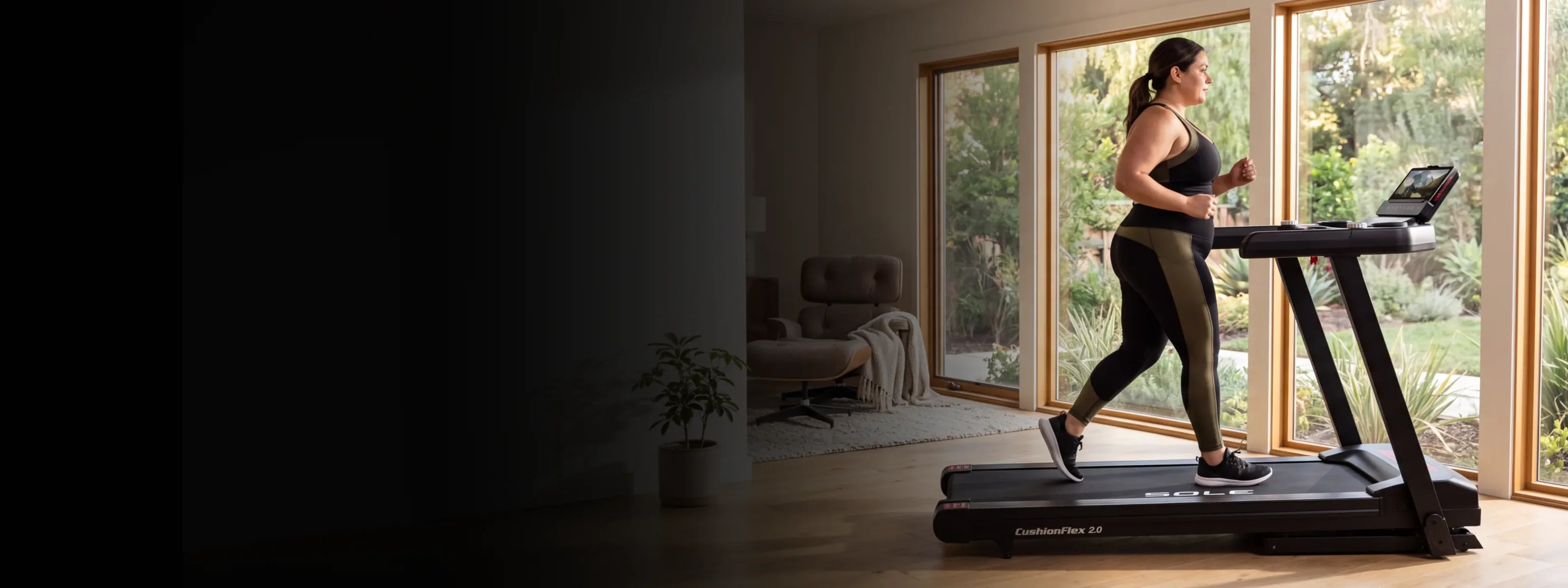 A runner on the SOLE F63 treadmill facing a wall of garden windows